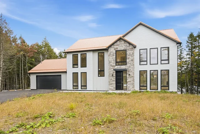 Modern two-storey home at 83 Canoe Crescent in Hammonds Plains, Nova Scotia, featuring white siding, stone accents, black-framed windows, a double garage, and a landscaped front lawn.