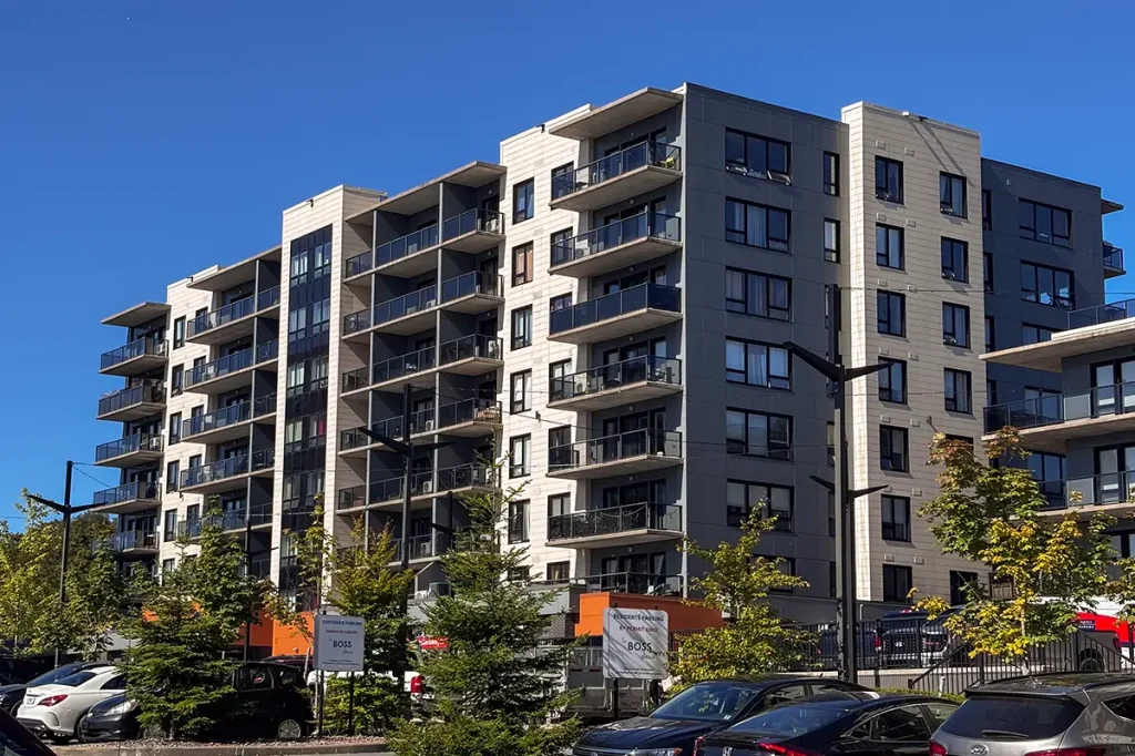 Exterior view of The Boss Plaza 2 apartment building in Fairview, Halifax, Nova Scotia, featuring modern architecture, glass-railed balconies, light and dark exterior cladding, and landscaped grounds.